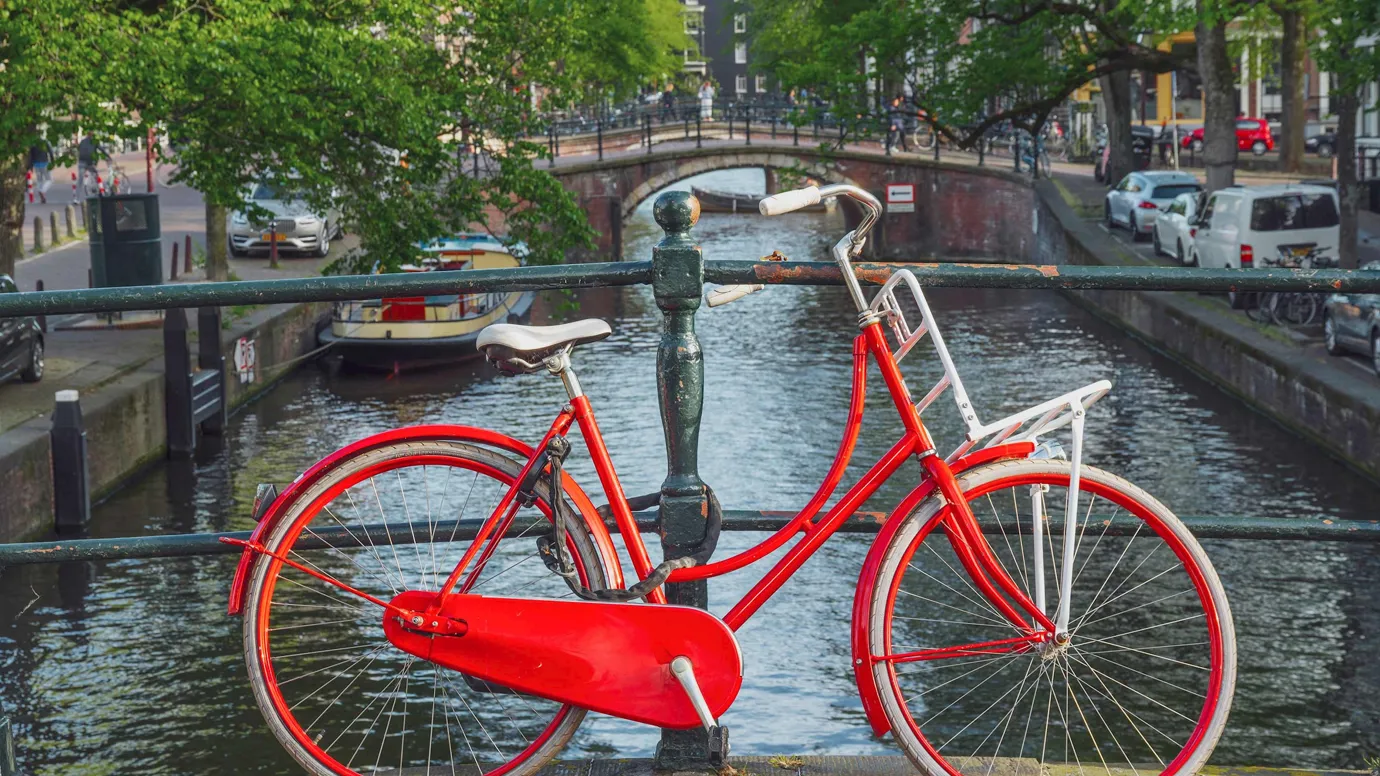 Bright red bicycle on a bridge overlooking canal and boats in Amsterdam, Netherlands