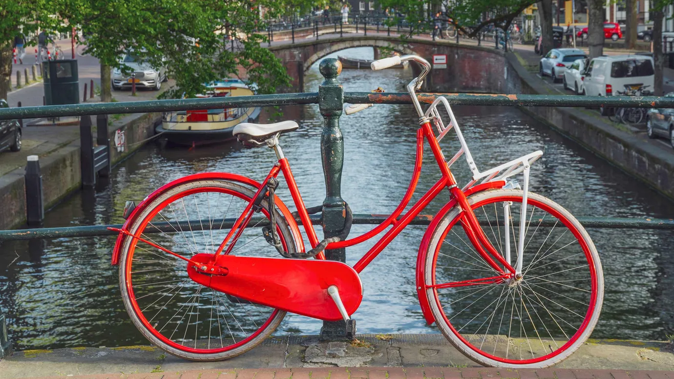 Bright red bicycle on a bridge overlooking canal and boats in Amsterdam, Netherlands