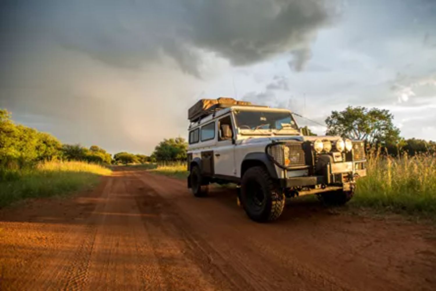 A jeep driving down a dirt road under a cloudy sky