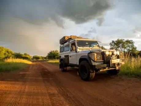 A jeep driving down a dirt road under a cloudy sky