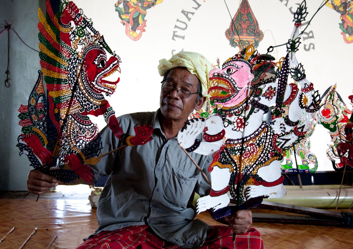 A man smiling at the camera with ornate puppets in Wayang Kulit Indonesia