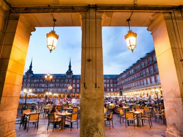 Outdoor dining area viewed through stone archway in Madrid, Spain