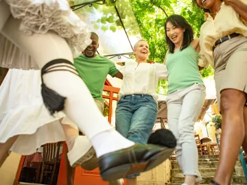 People performing traditional Greek dance in outdoor setting with greenery, Athens, Greece