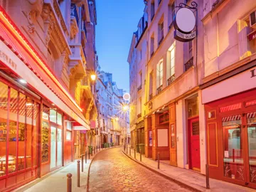 External view of a narrow cobblestone street illuminated by vibrant neon lights in Paris, France