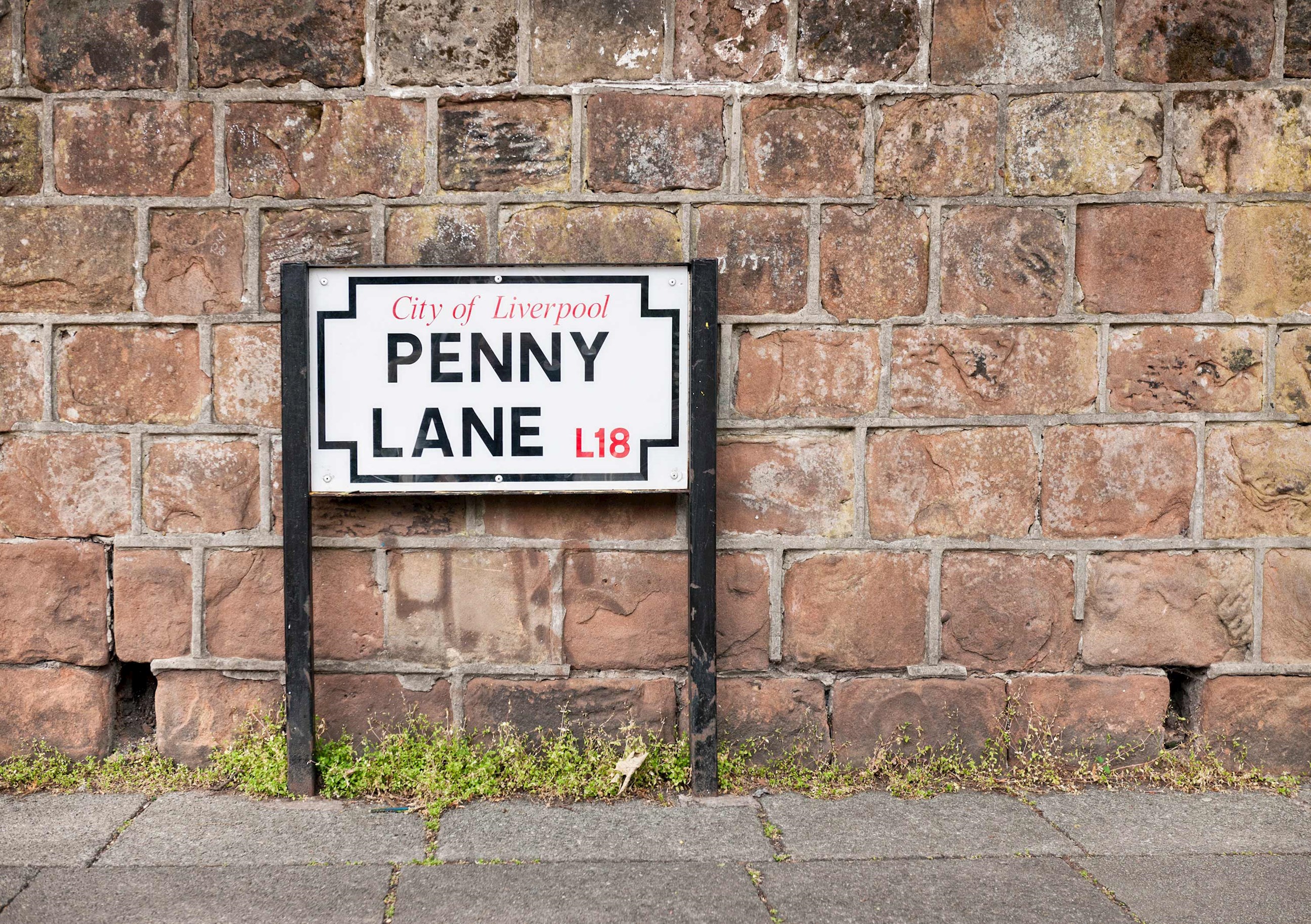 Penny Lane street sign mounted on black posts by brick wall in Liverpool, England