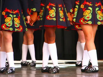 Irish dancers wearing black dresses with colourful Celtic patterns and soft shoes.