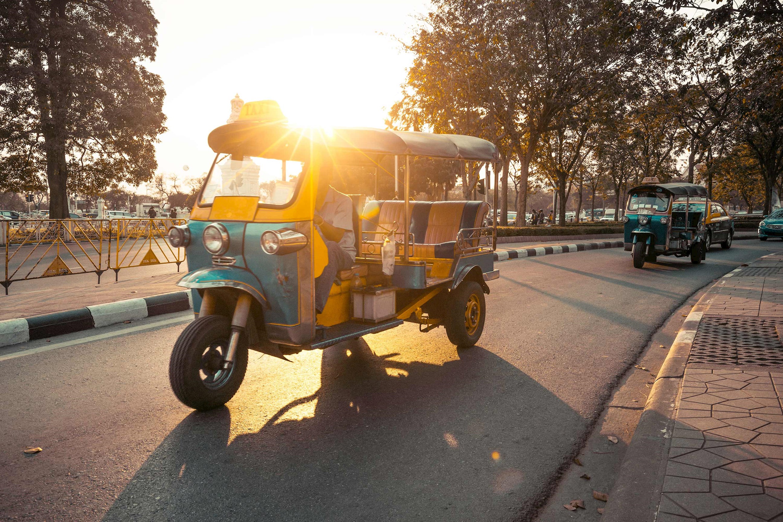 Tuk-tuk driving on sunlit street with trees in Bangkok, Thailand
