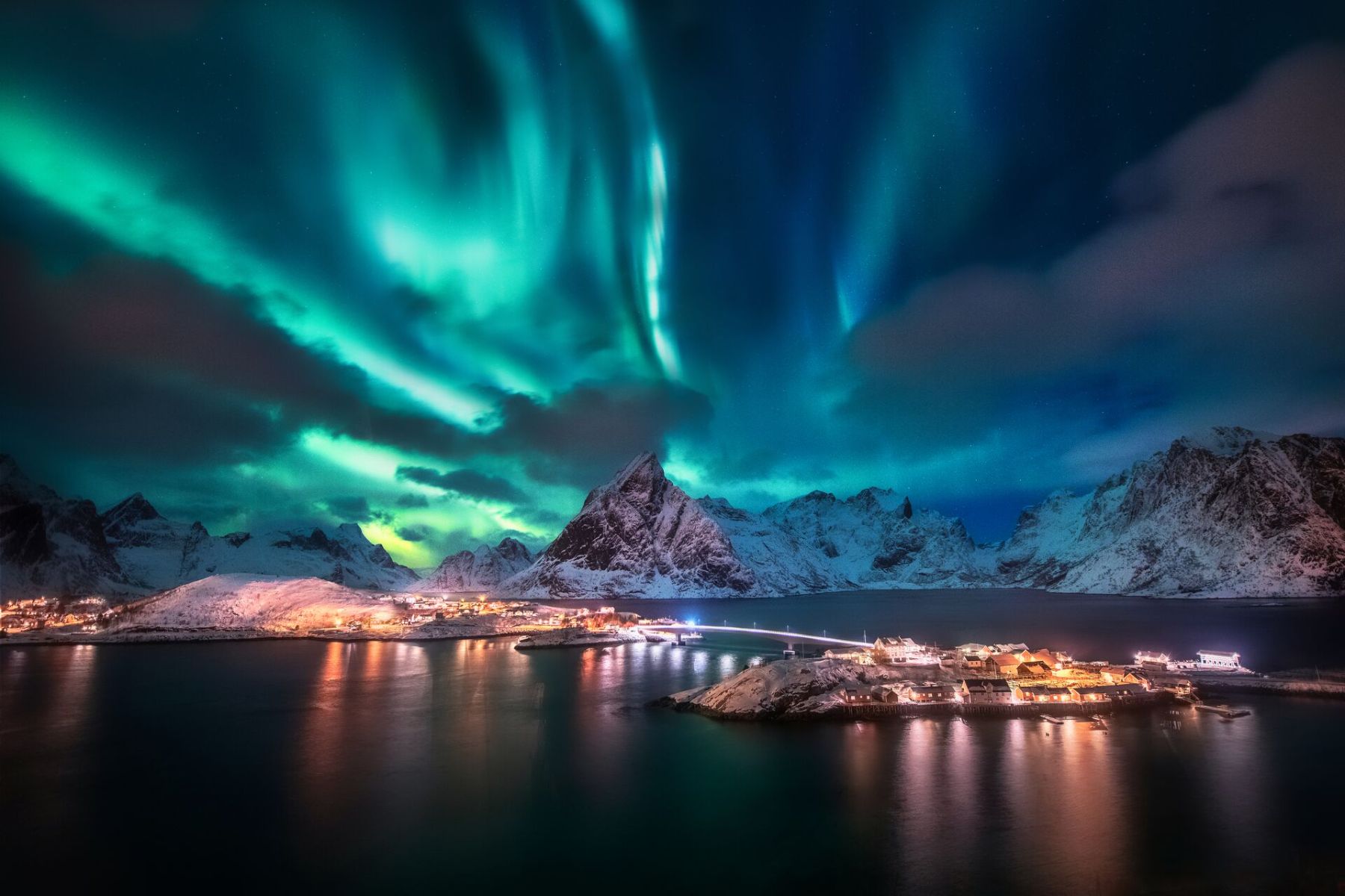 The Northern Lights over snow covered mountains by water in the Lofoten Islands, Norway