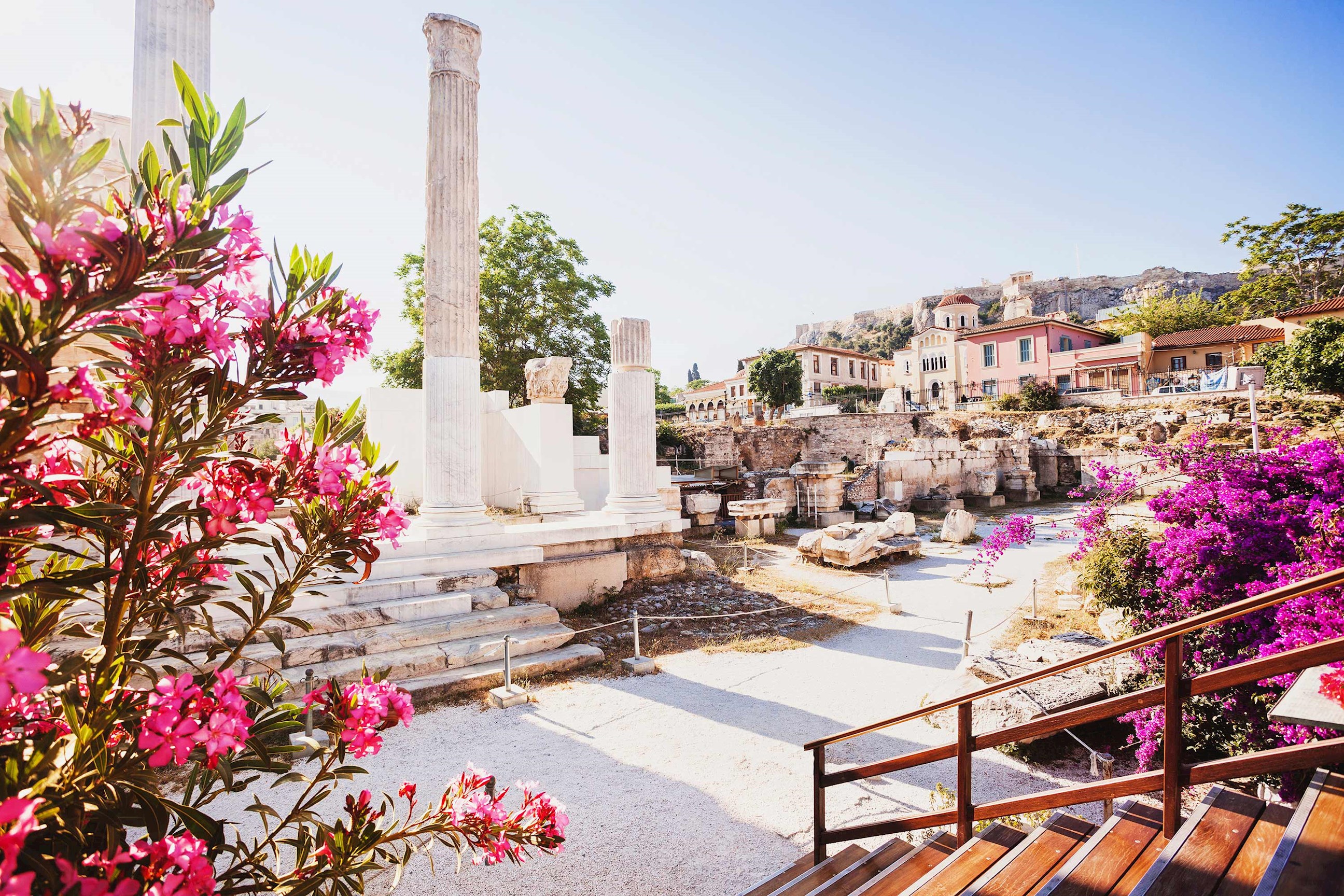 Hadrian’s Library ruins with pink flowers and Acropolis in background in Athens, Greece