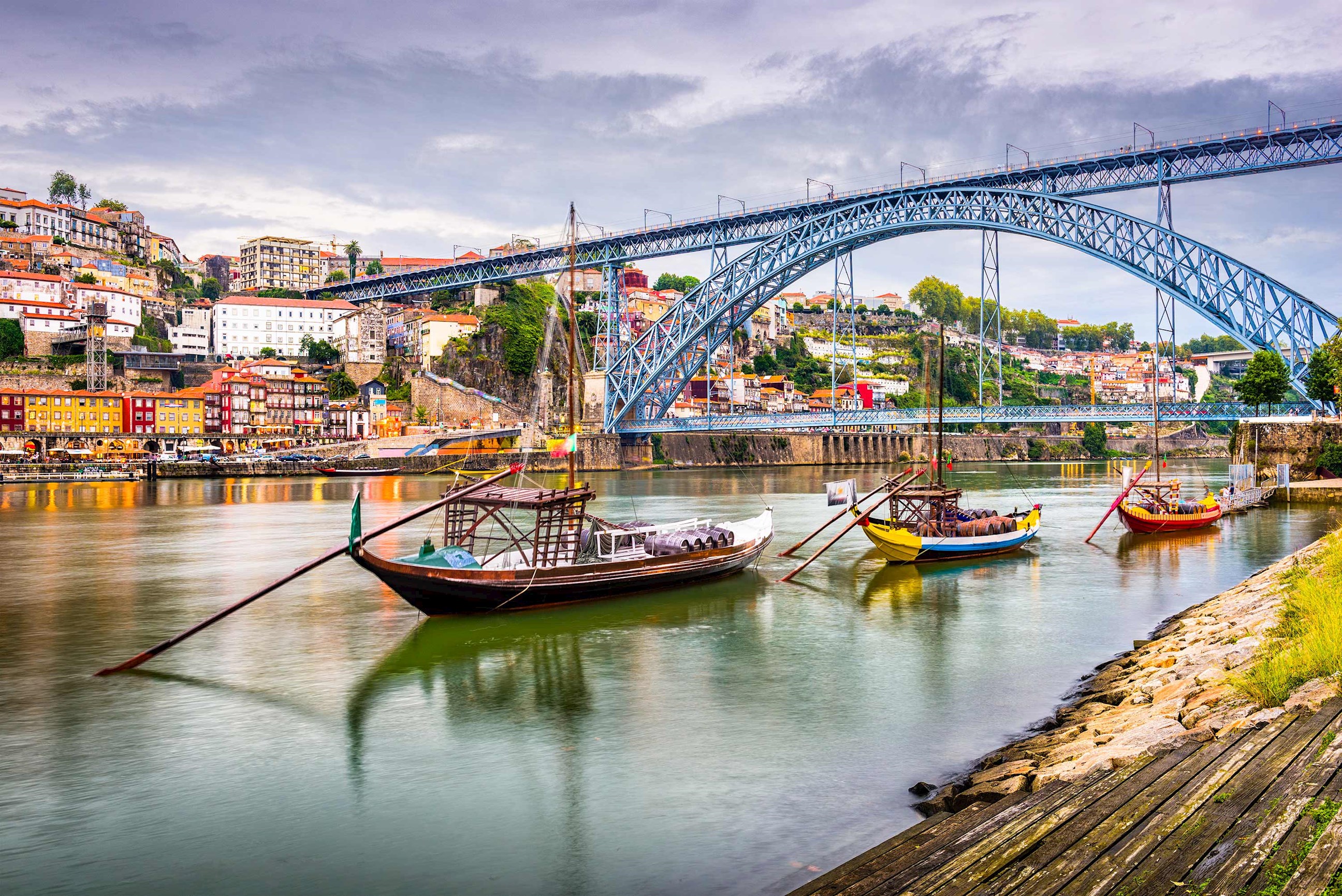 Traditional wooden boats beneath large metal bridge in Porto, Portugal
