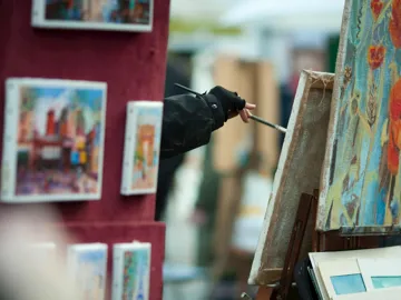 A person painting on a canvas surrounded by paintings in Paris, France