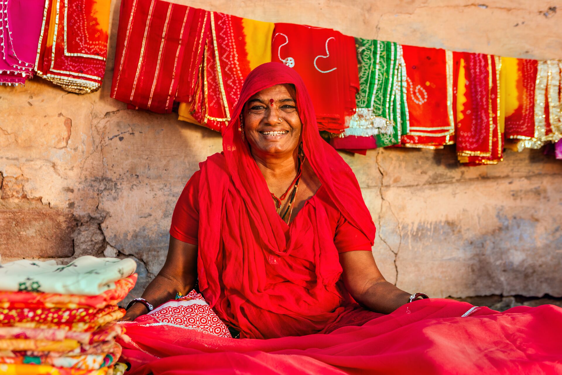 Indian Woman sat on floor amidst the colourful fabrics she's selling in India