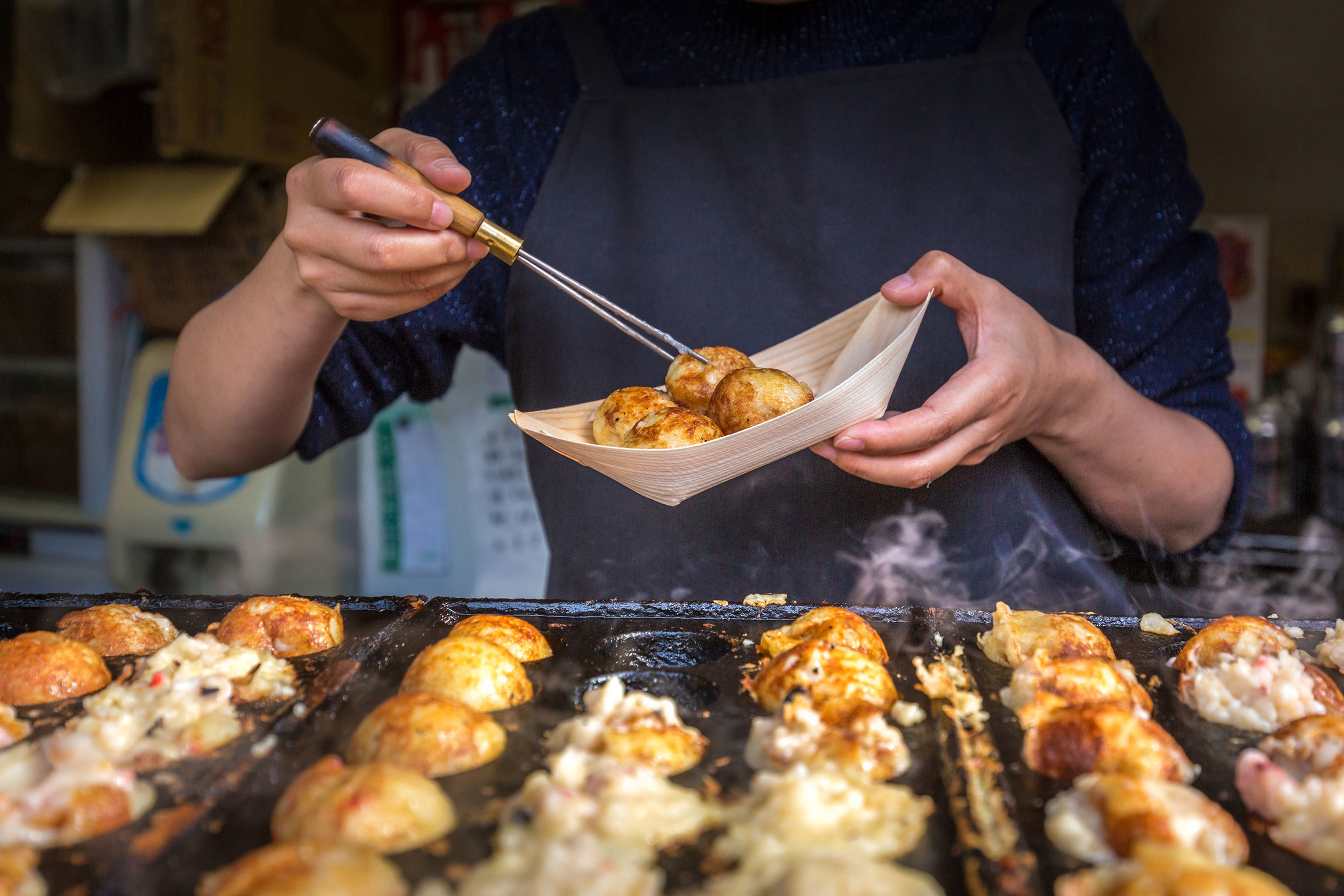 Close-up of vendor serving freshly cooked takoyaki from hot griddle