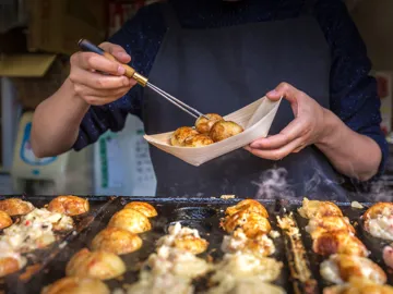 Close-up of vendor serving freshly cooked takoyaki from hot griddle