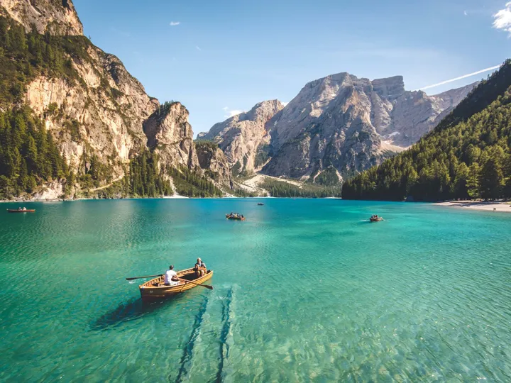 Small boats on a lake with clear water, surrounded by mountains.