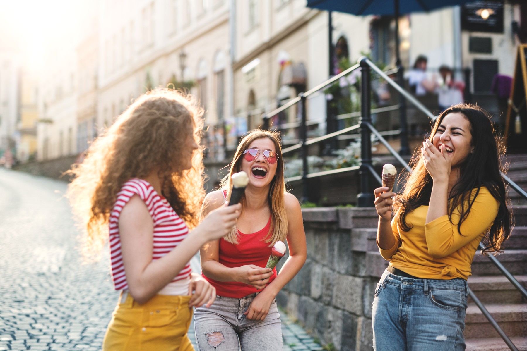 Three Cheerful Female Teenager Friends With Ice Cream Standing On The Street, Laughing