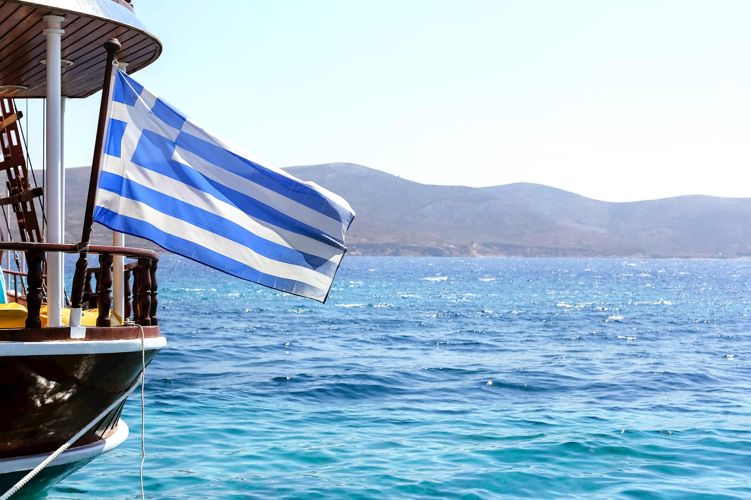 Greek flag on boat with blue sea and distant mountains