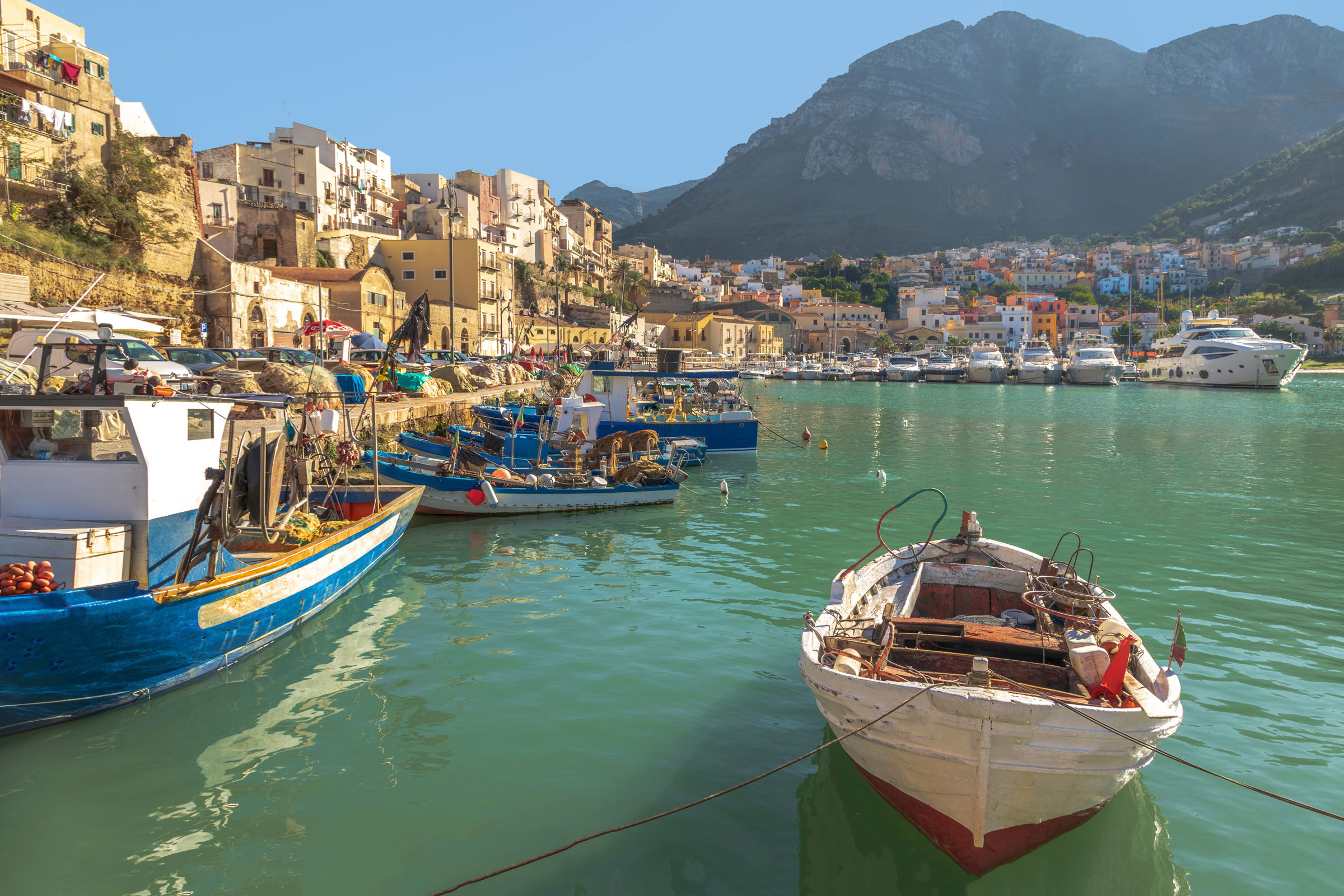 Close view of fishing boats in a turquoise harbour surrounded by hillside houses in Naples, Italy