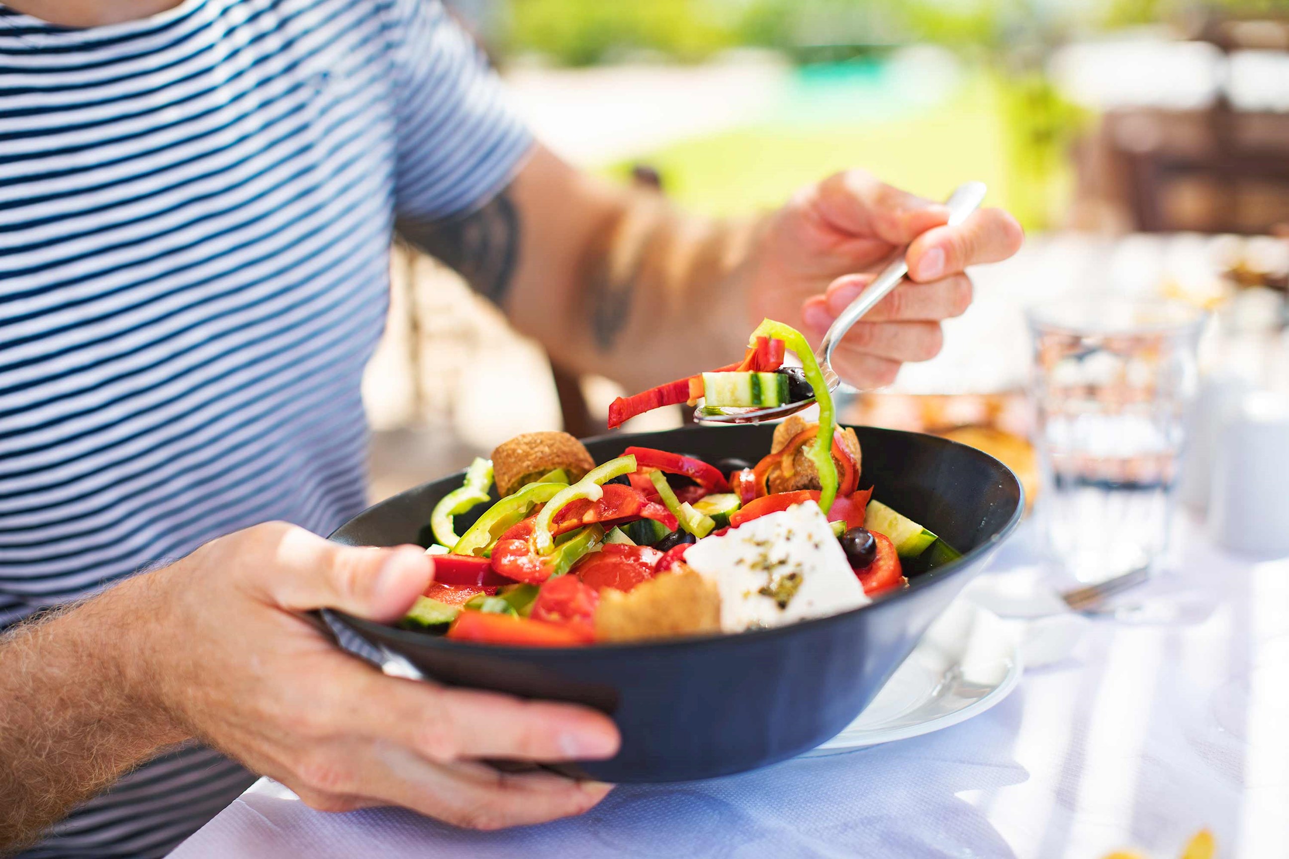 Close-up of hands holding a bowl of Greek salad 