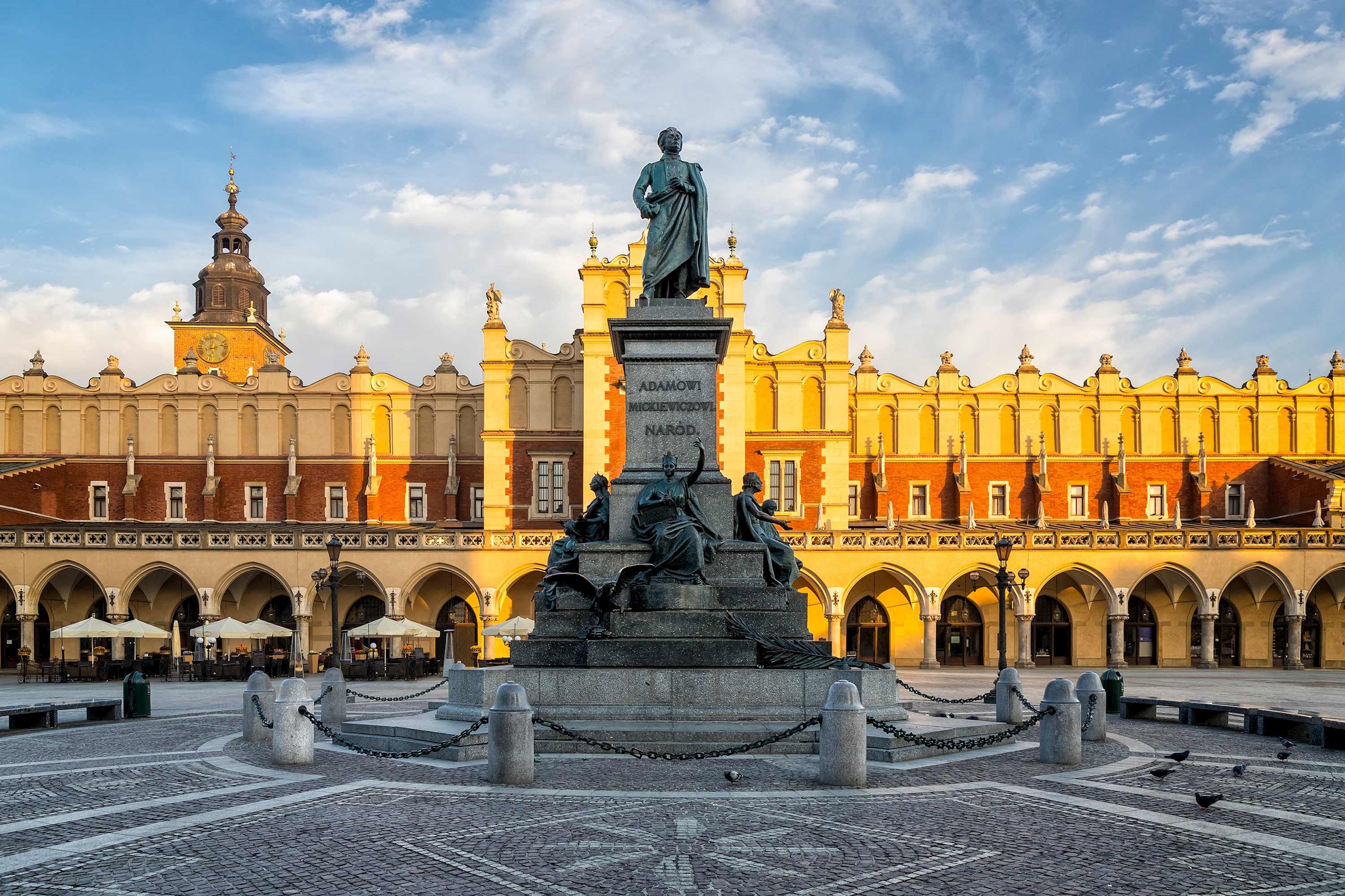 Statue in large square with historic building and arches behind in Krakow, Poland