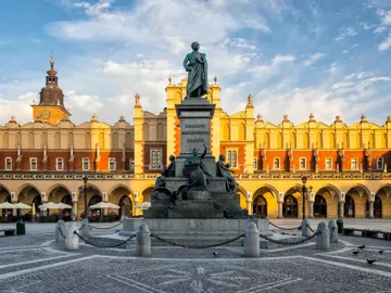 Statue in large square with historic building and arches behind in Krakow, Poland