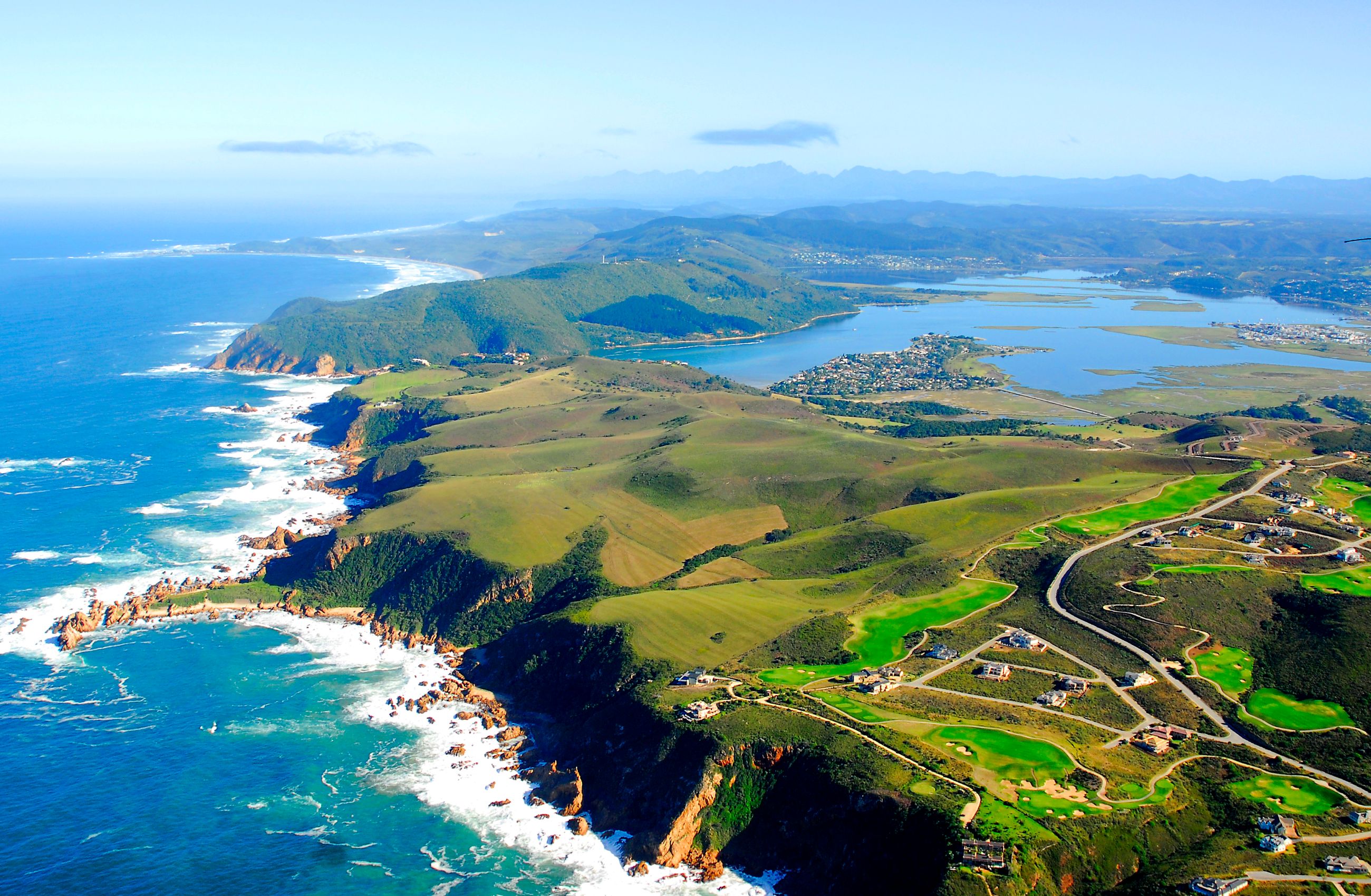 An aerial view of Knysna in South Africa showing rolling green country with a dramatic coastline.