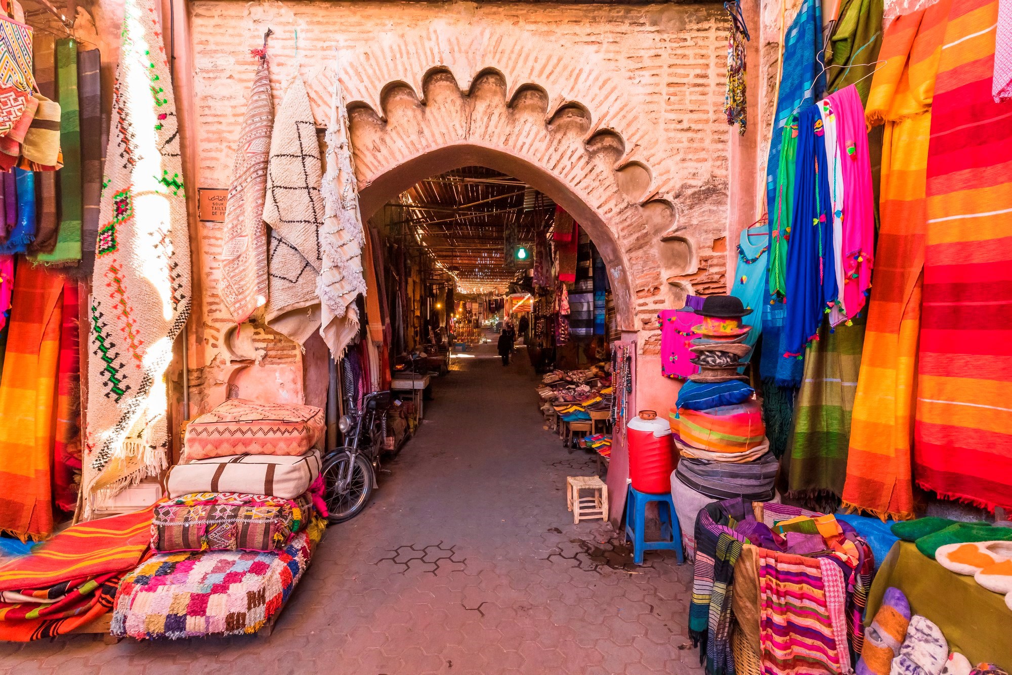 Colourful textiles and rugs displayed at an arched entrance to a Moroccan souk
