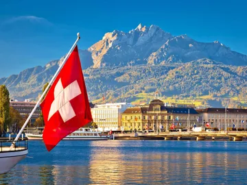 Swiss flag on boat with Lucerne waterfront and Mount Pilatus backdrop in Switzerland