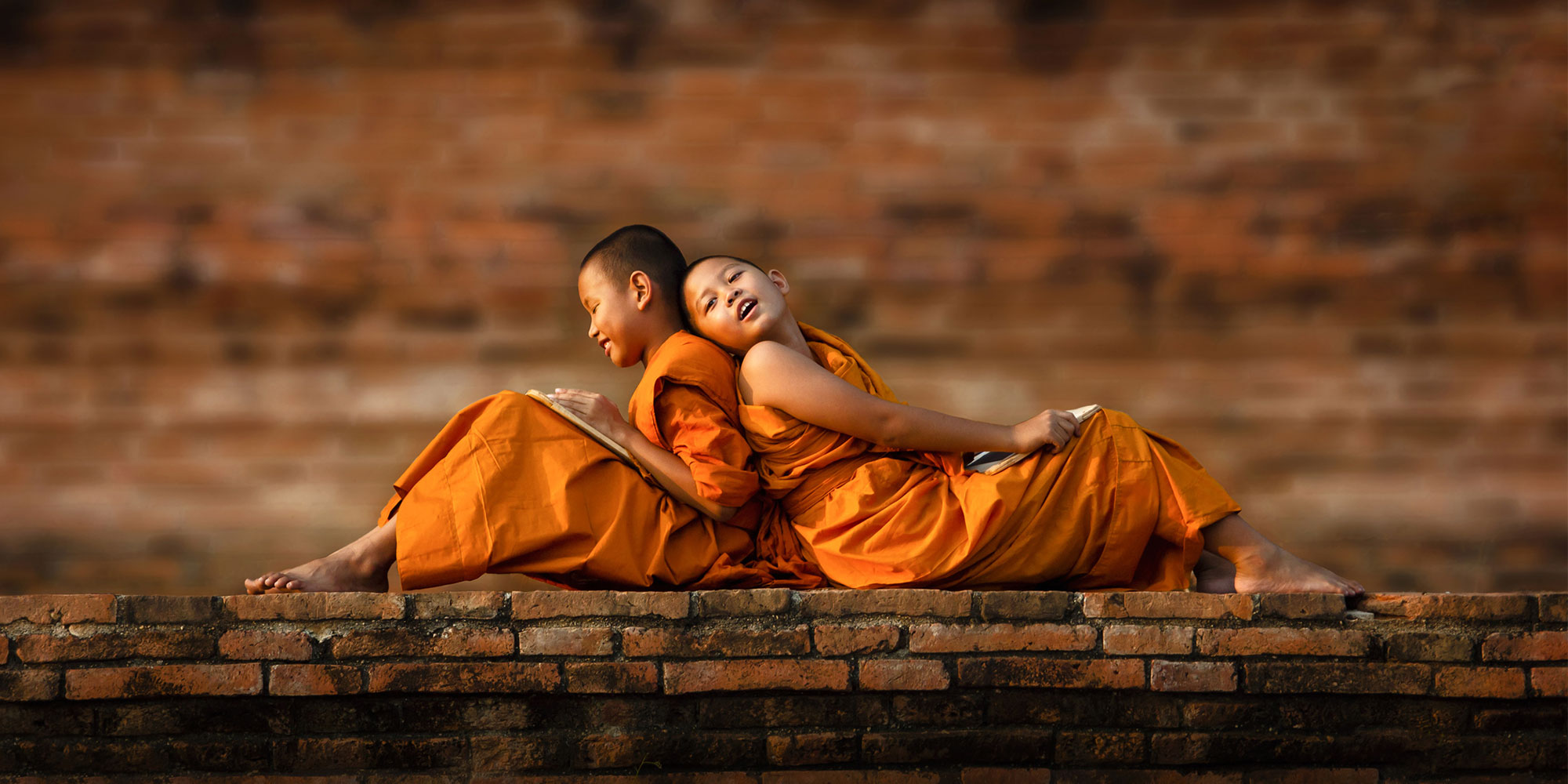 Young monks in traditional orange dress sat on a wall