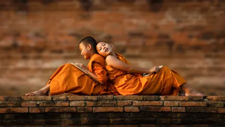 Young monks in traditional orange dress sat on a wall