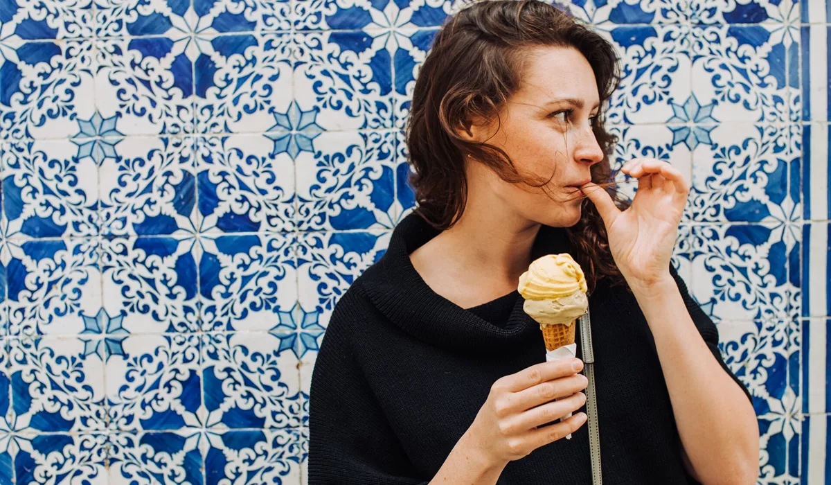 Millennial Woman Licking Finger While Eating Ice Cream At A Tiled Wall 