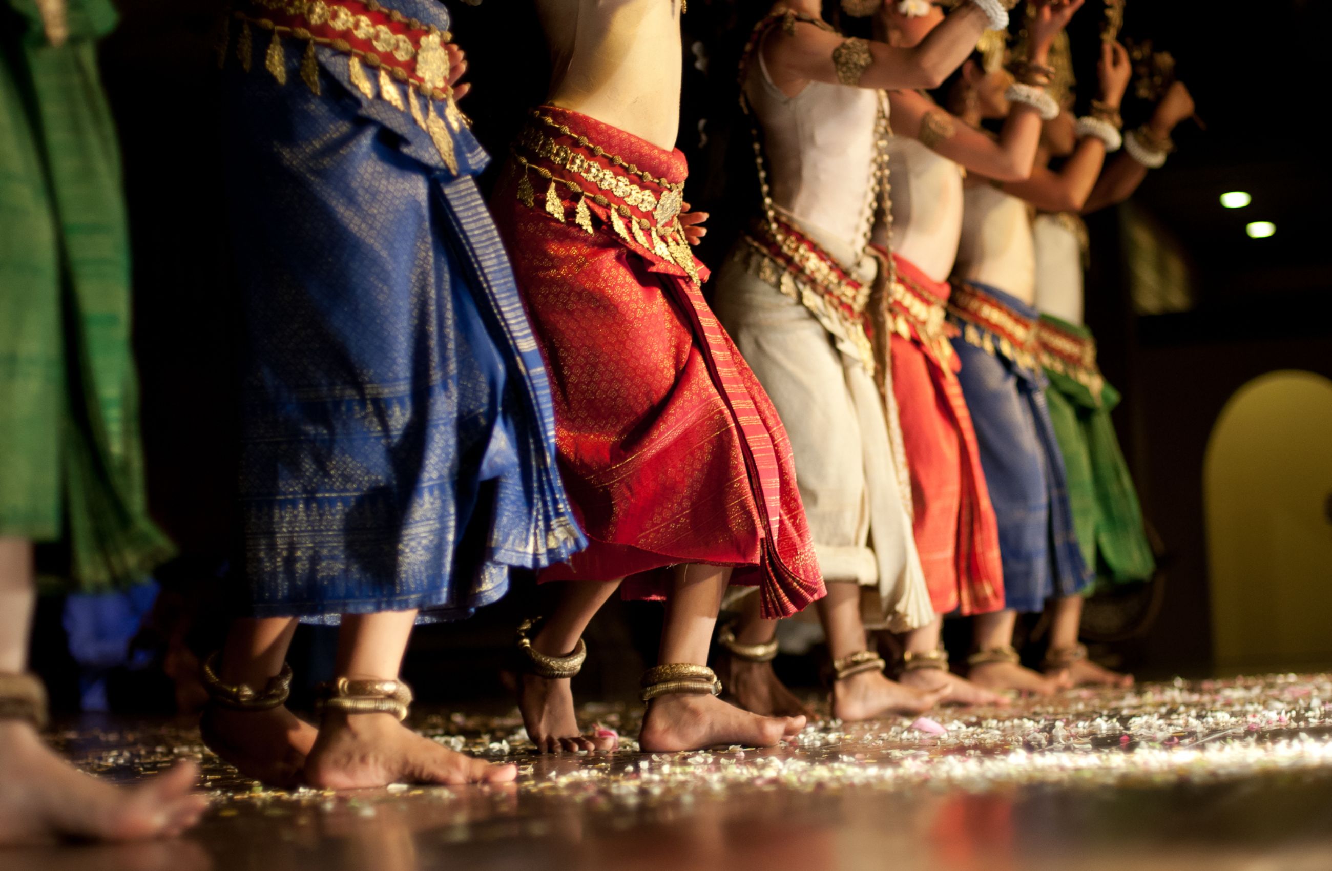 A line of Cambodian Apsara Dancers wearing colourful skirts, gold belts and many bangles around their ankles and wrists.