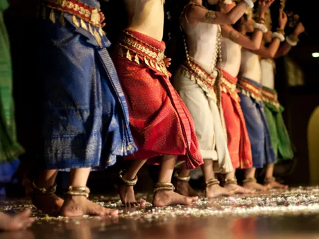 A line of Cambodian Apsara Dancers wearing colourful skirts, gold belts and many bangles around their ankles and wrists.