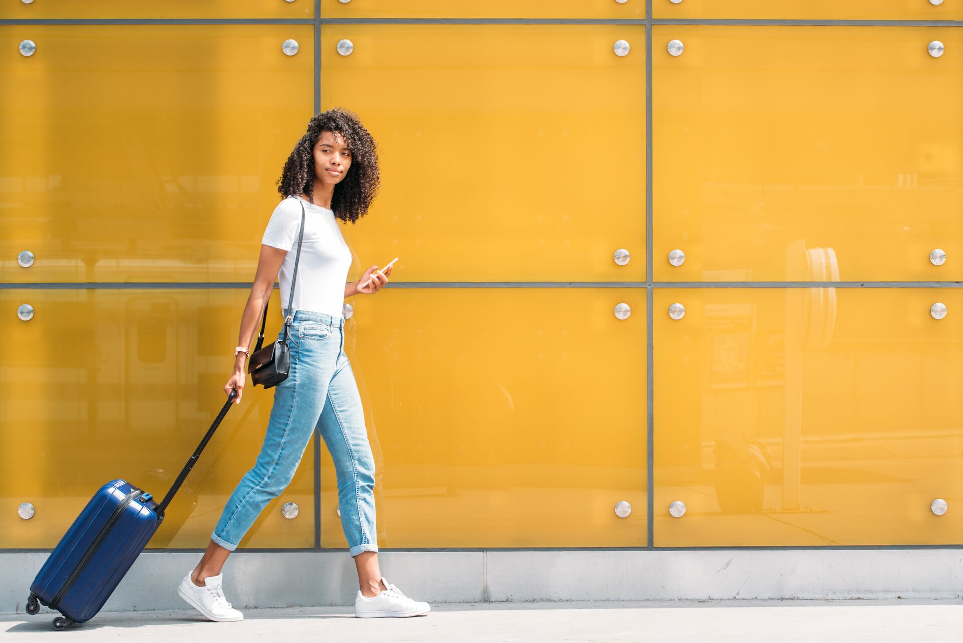 Woman with suitcase walking past a yellow wall
