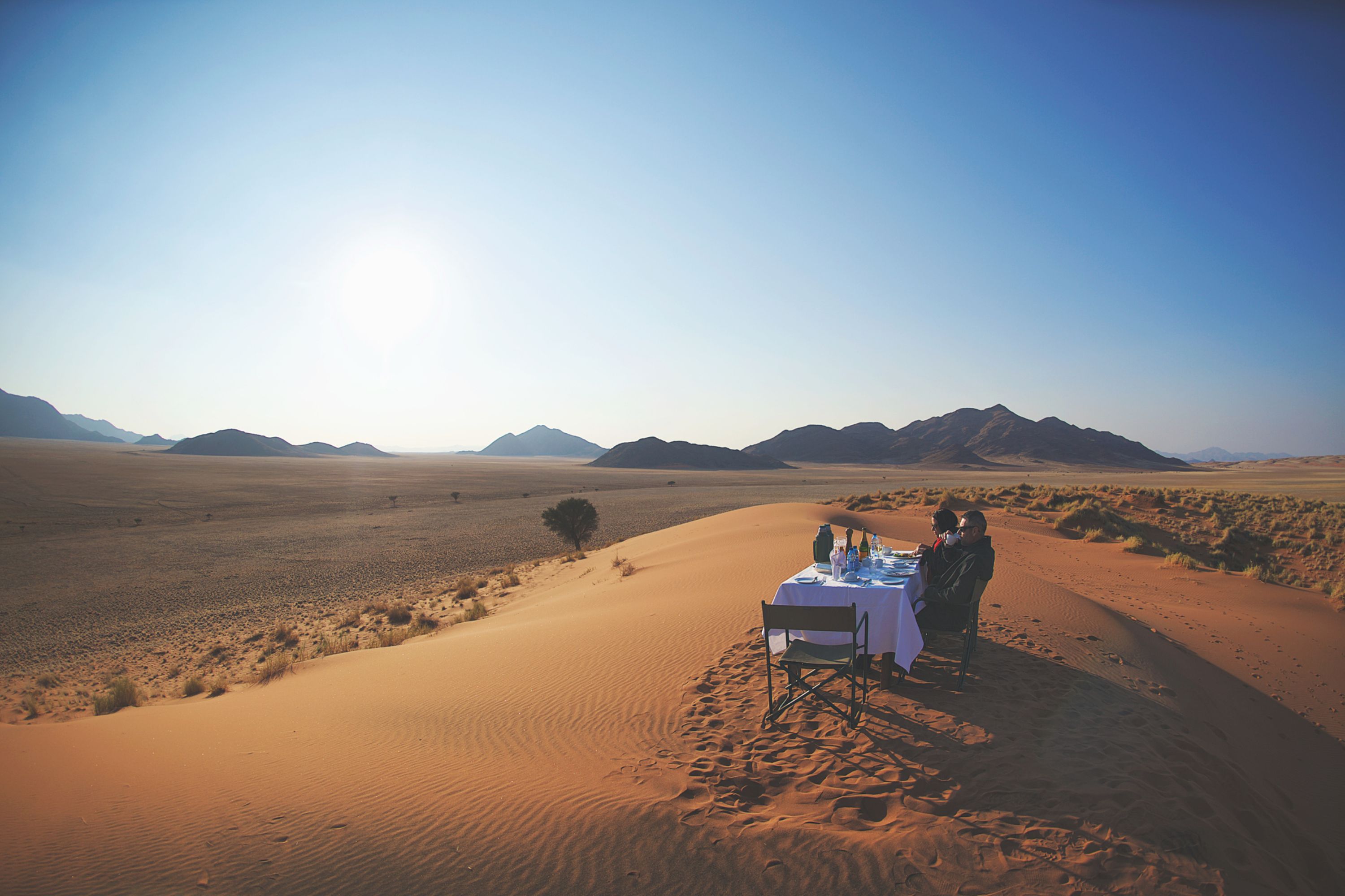 Two people sitting at a single table on a sand dune in Namibia