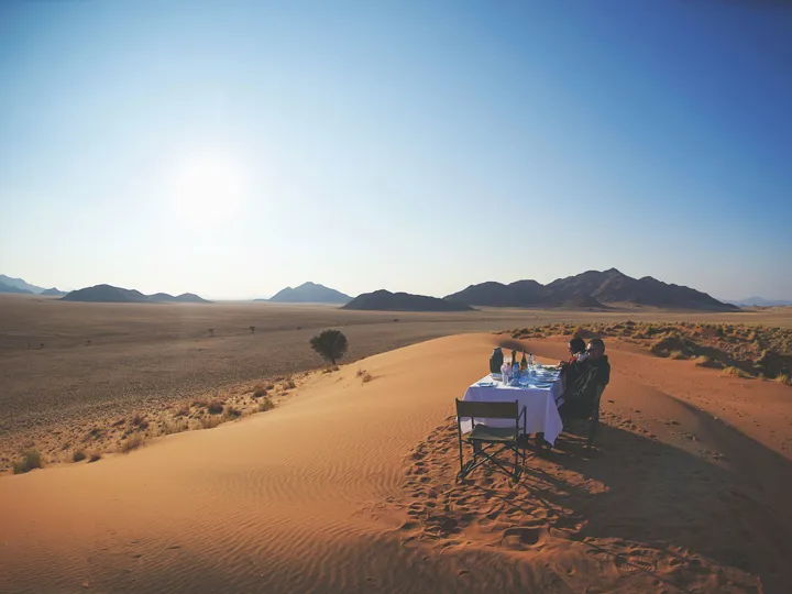 Two people sitting at a single table on a sand dune in Namibia