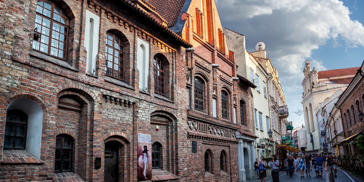 A group of people walking down a street next to tall buildings Lithuania Pilies Street