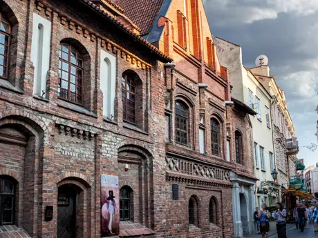 A group of people walking down a street next to tall buildings Lithuania Pilies Street