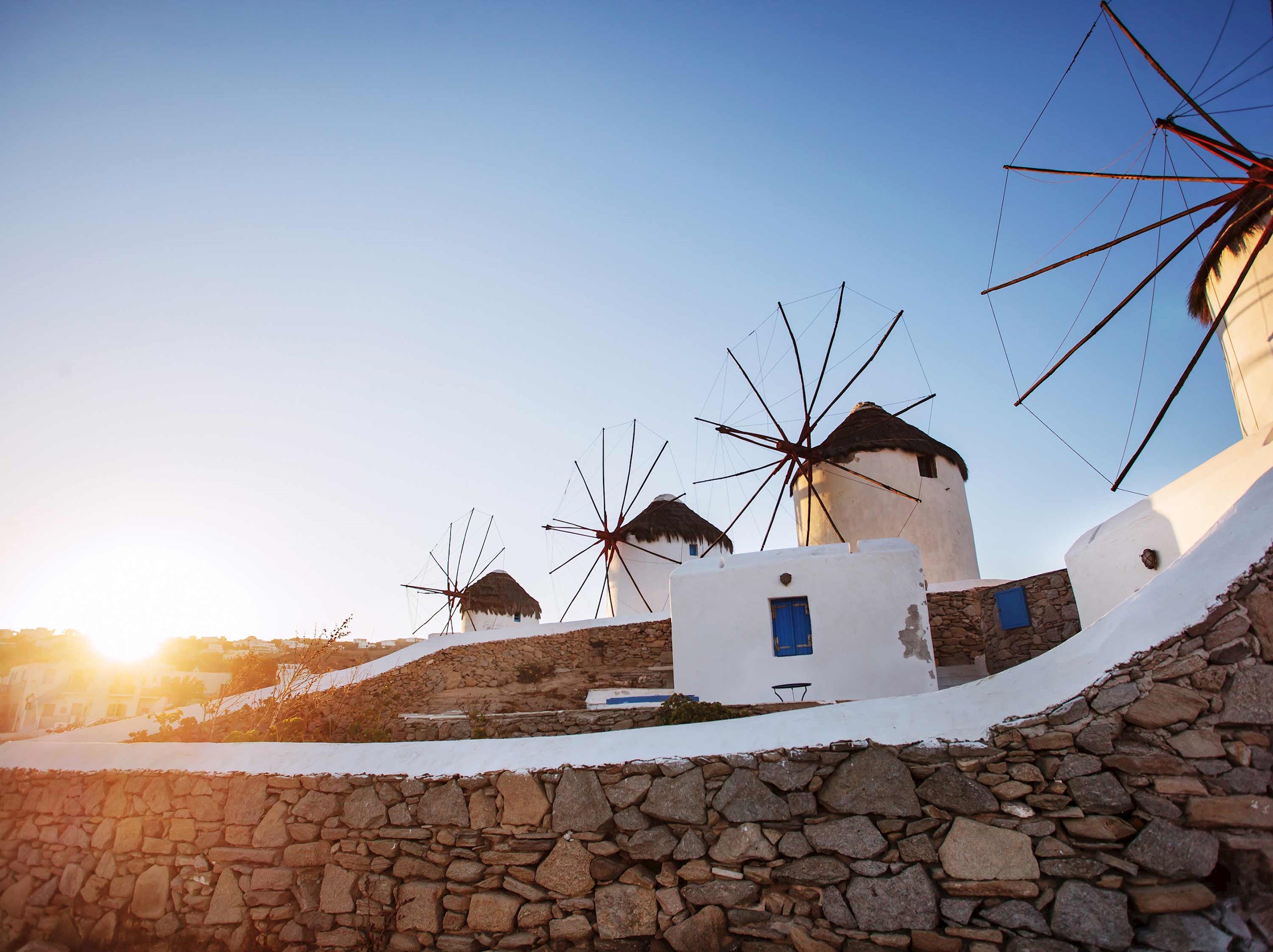 Iconic white windmills of Mykonos on stone wall at sunset