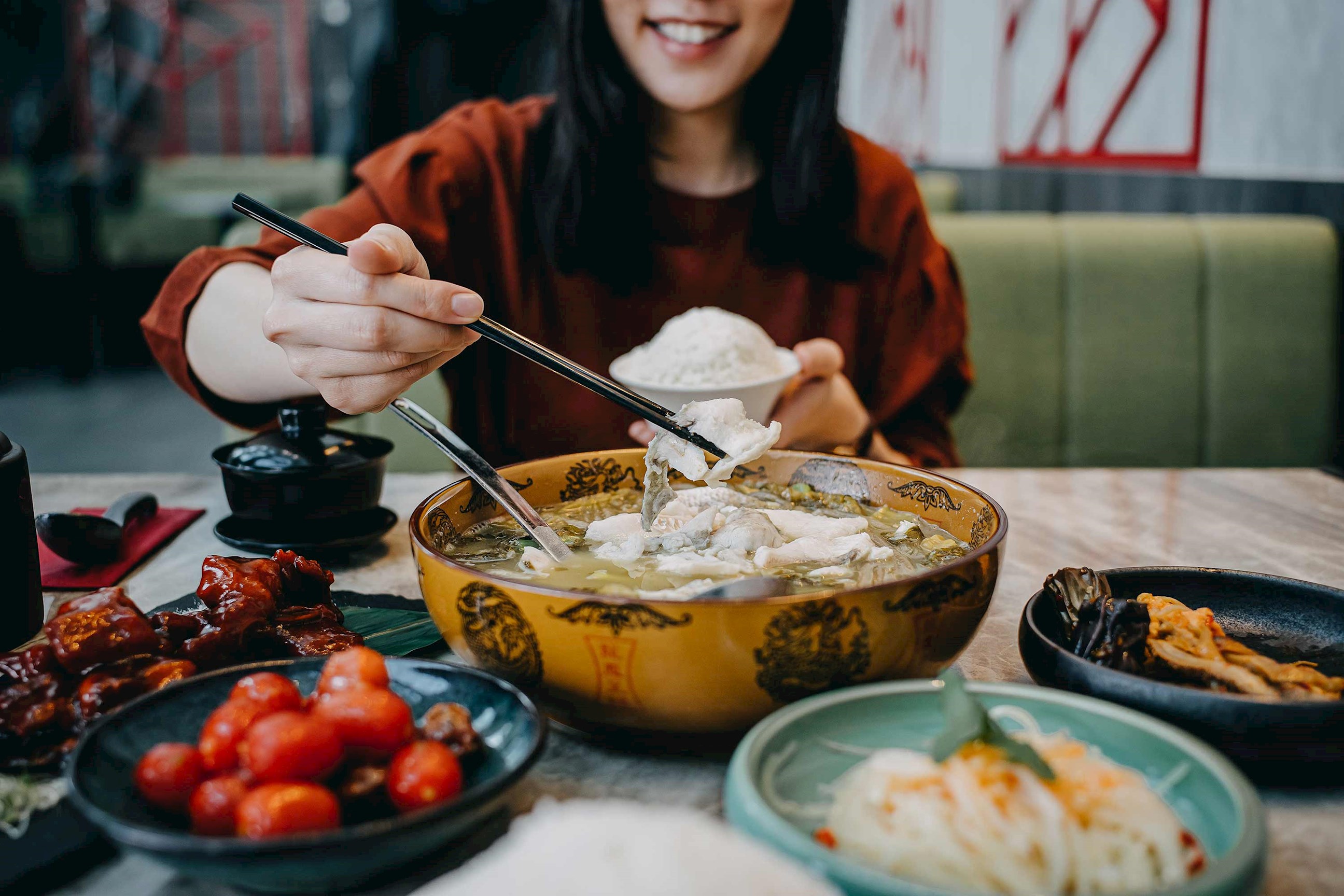 Close-up of person using chopsticks to pick fish from soup bowl 