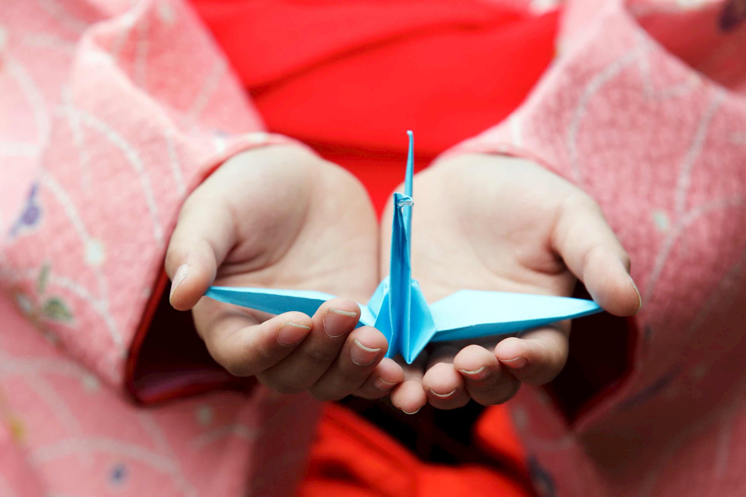 Close-up of hands holding blue origami crane