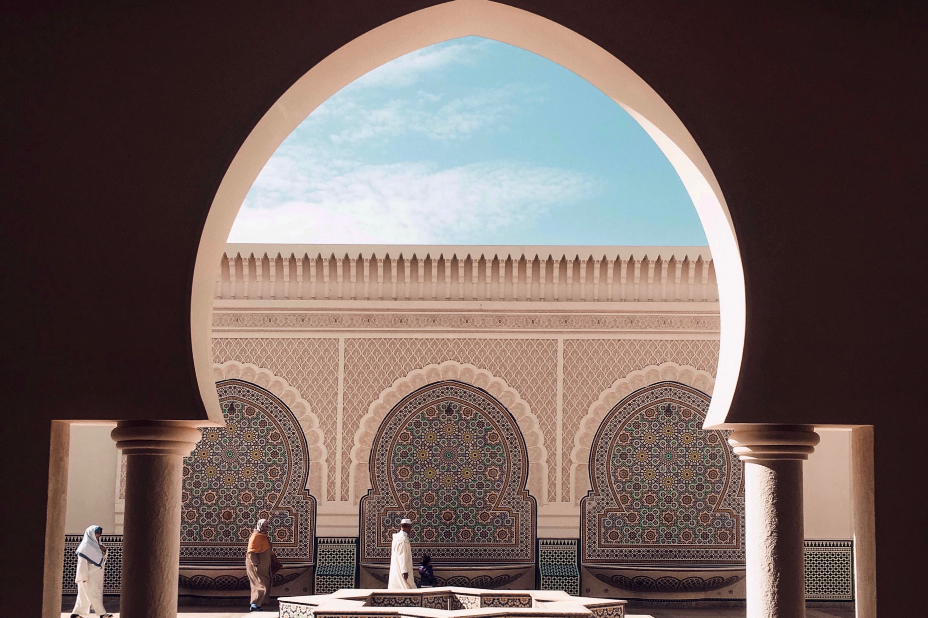 An archway in the foreground with intricate tiled walled in the background in Fez Medina in Morocco.