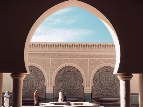 An archway in the foreground with intricate tiled walled in the background in Fez Medina in Morocco.