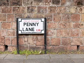 Penny Lane street sign mounted on black posts by brick wall in Liverpool, England