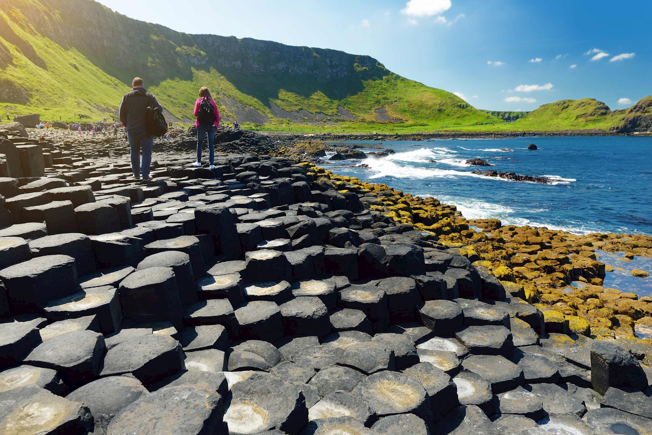 People walking on a rock formations near ocean coastline in Giant's Causeway