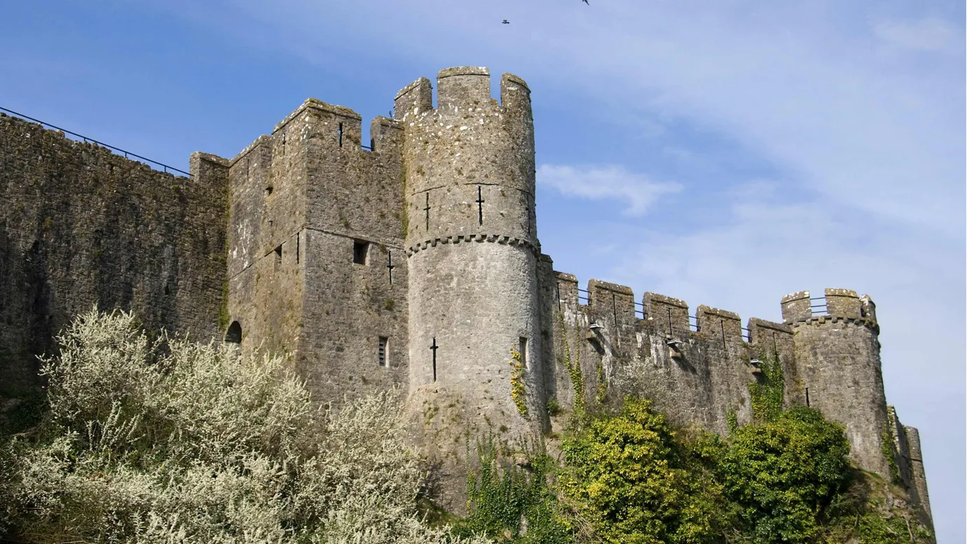 Stone castle with round towers surrounded by trees in Pembroke, Wales