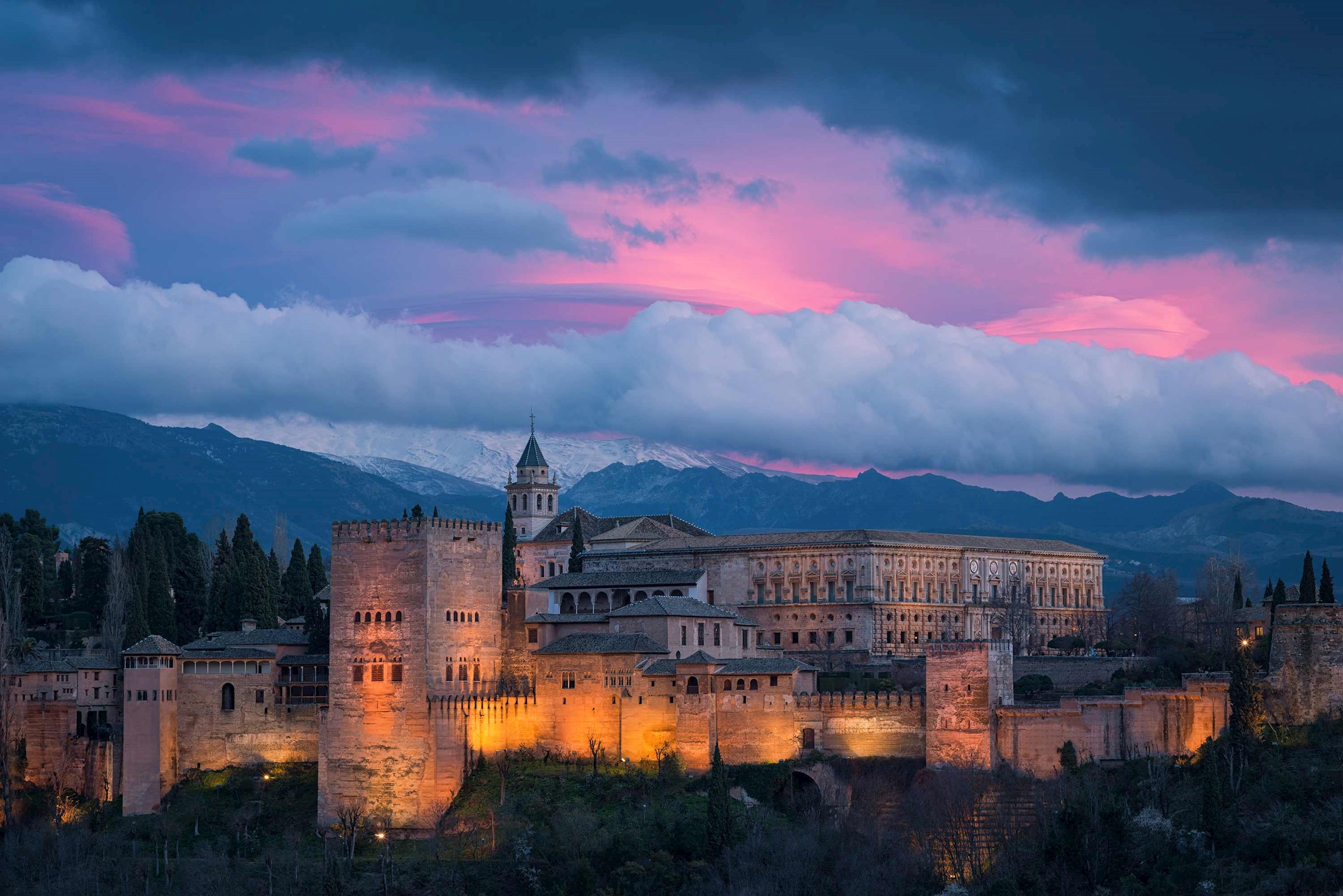Illuminated towers at dusk under dramatic pink sky in Granada, Spain
