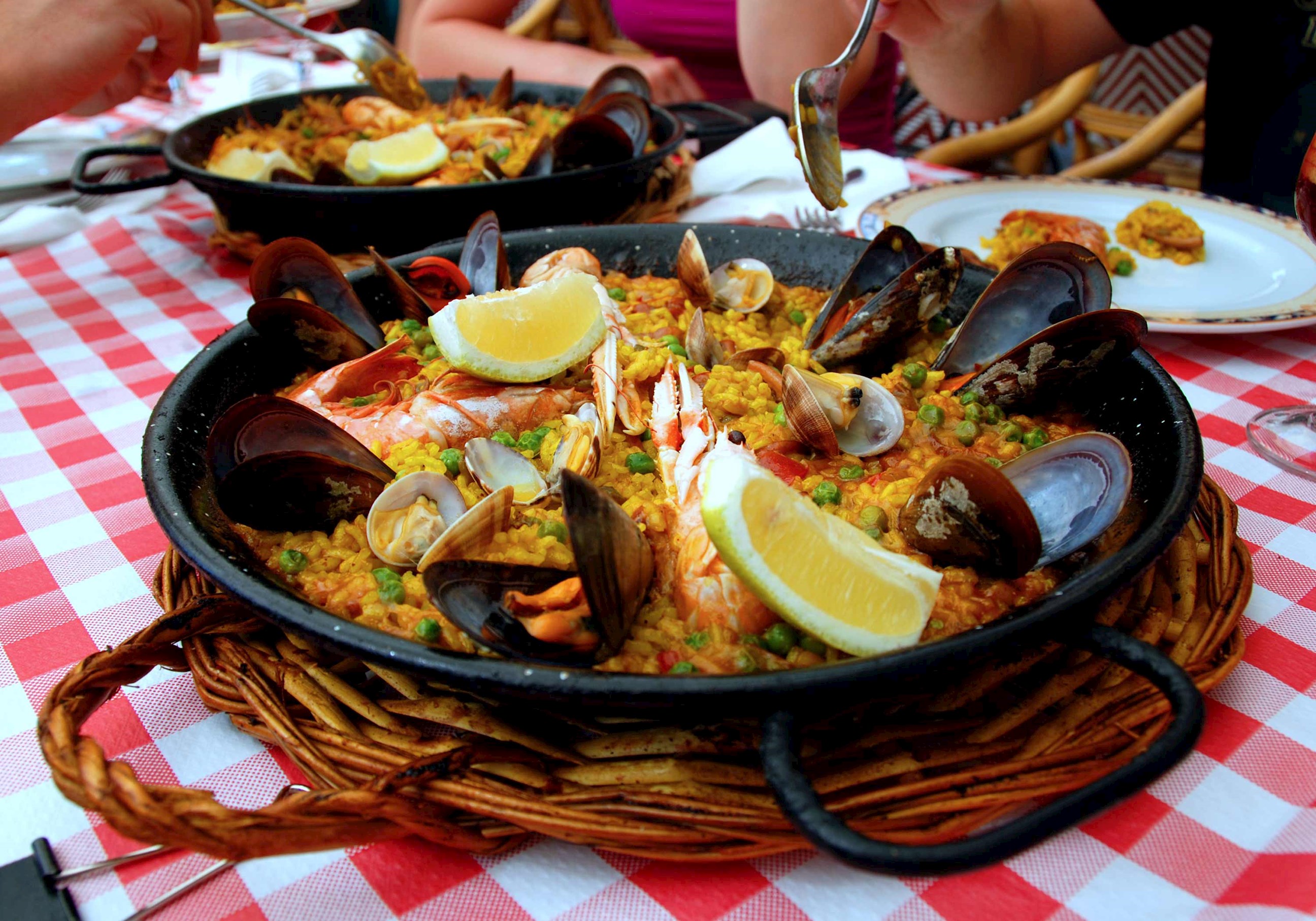 Seafood paella served in a black pan with mussels, clams, shrimp and lemon wedges on a checkered tablecloth