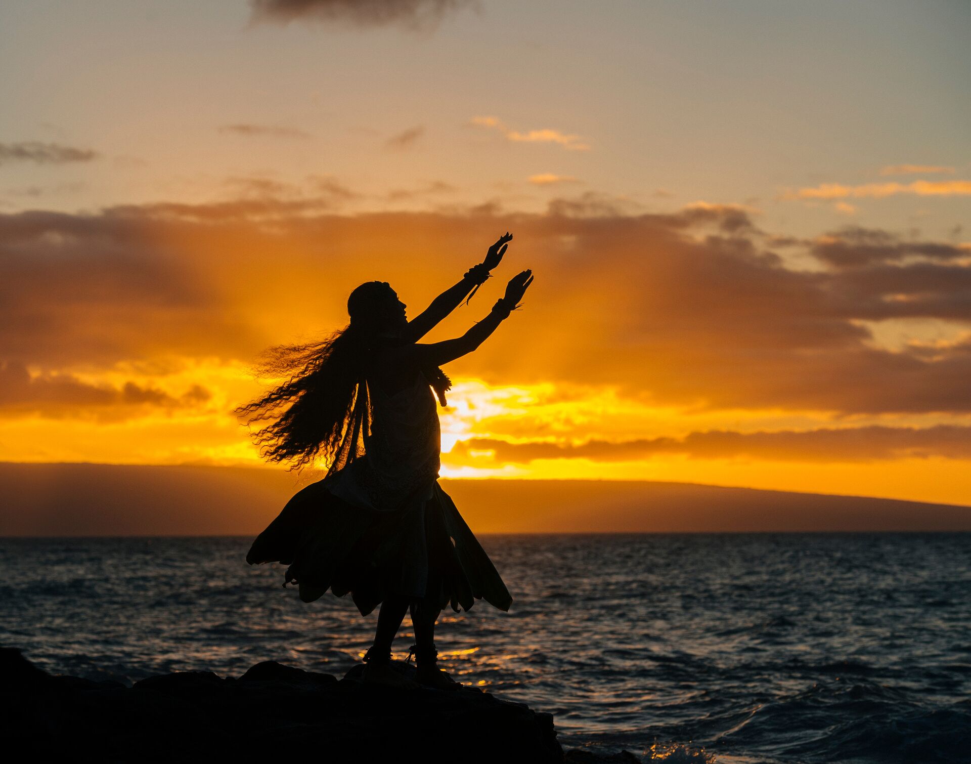 large-silhouetted-young-woman-in-traditional-costume-hula-dancing-on-coastal-rock-at-sunset-maui-hawaii-usa-558963001-1.jpg