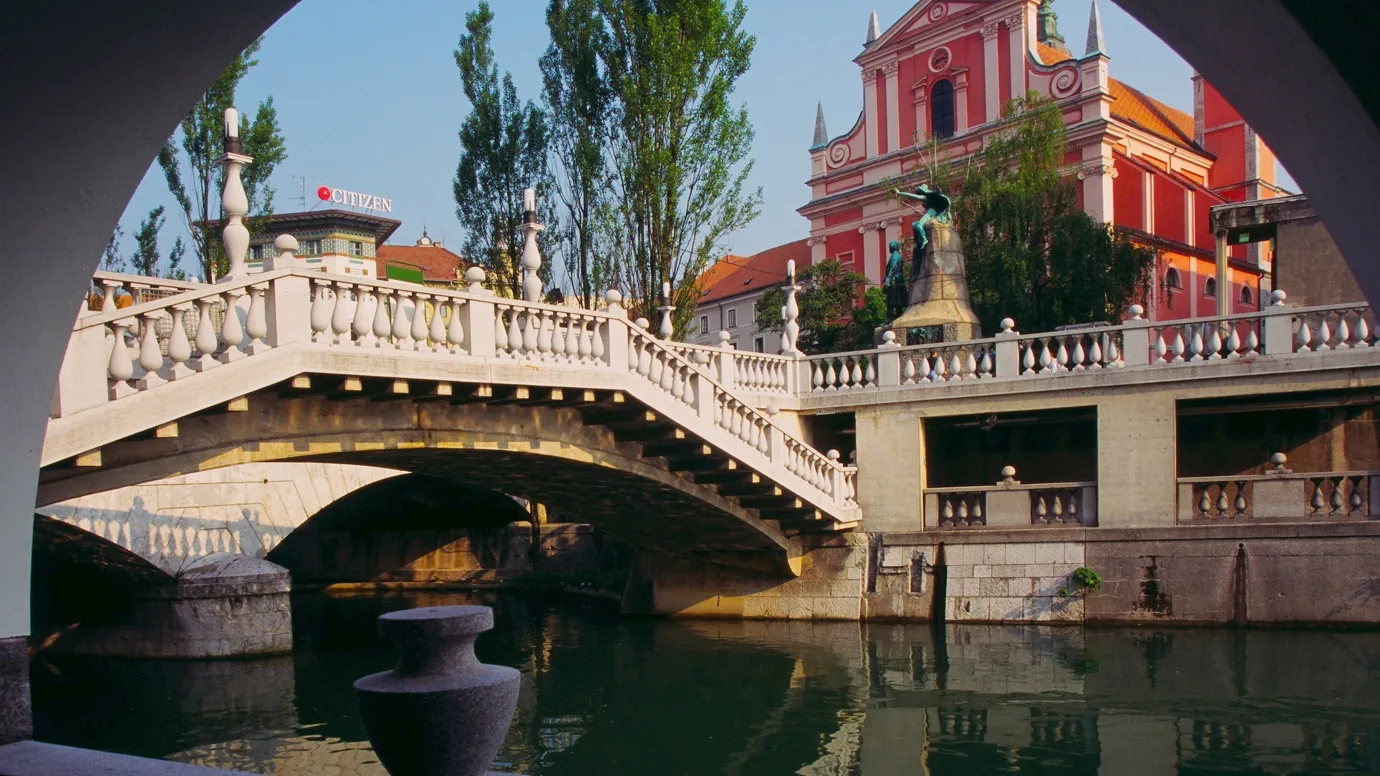 A riverside arch view of a bridge and pink building in Ljubljana, Slovenia